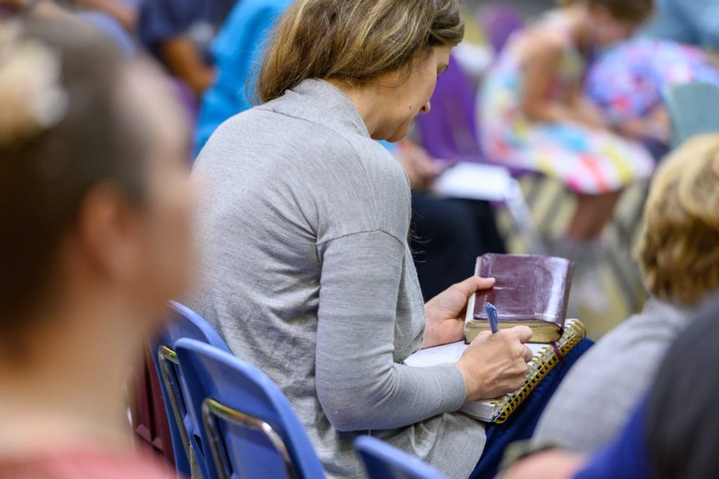 Woman writing notes from the sermon while holding a Bible.